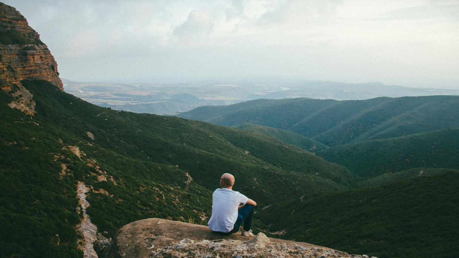 person sitting on the edge of a cliff over looking mountains during daytime showing sustainable sports