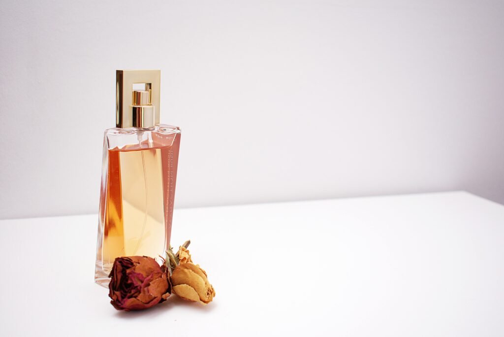 Elegant glass perfume bottle with luxurious design placed next to dried flowers against a minimalistic white background. Indian perfume industry