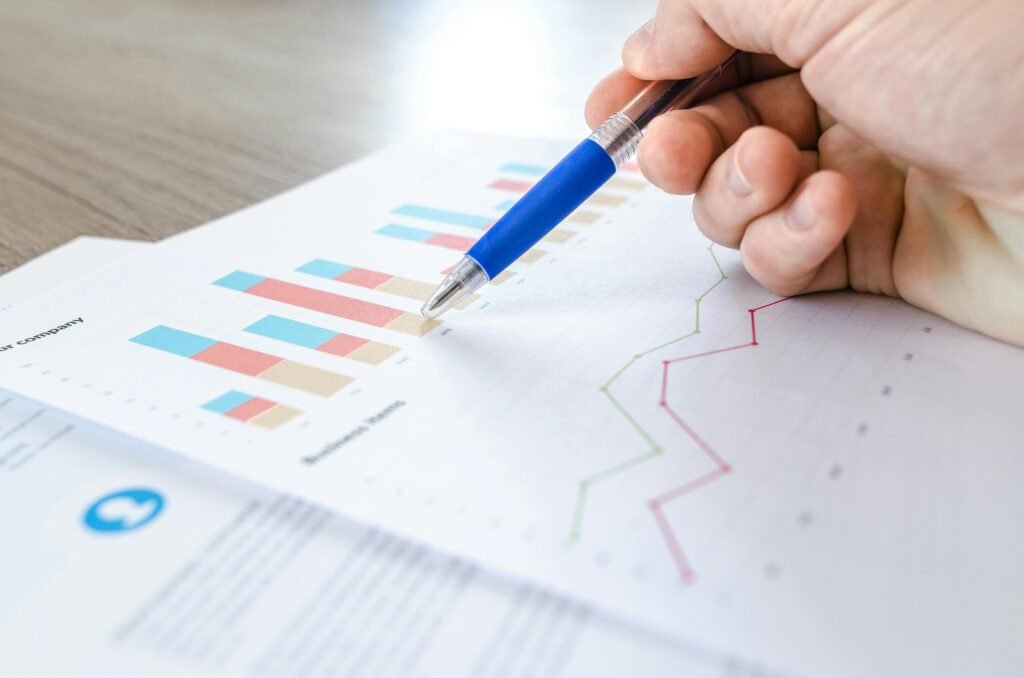 A close-up of a hand with a pen analyzing data on colorful bar and line charts on paper. Big data in Climate Prediction