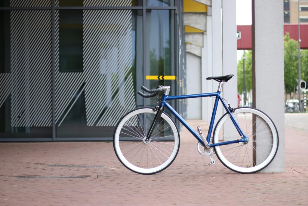 A sleek blue bicycle parked against a modern glass building's exterior in an urban setting. To show bicycle friendly cities.