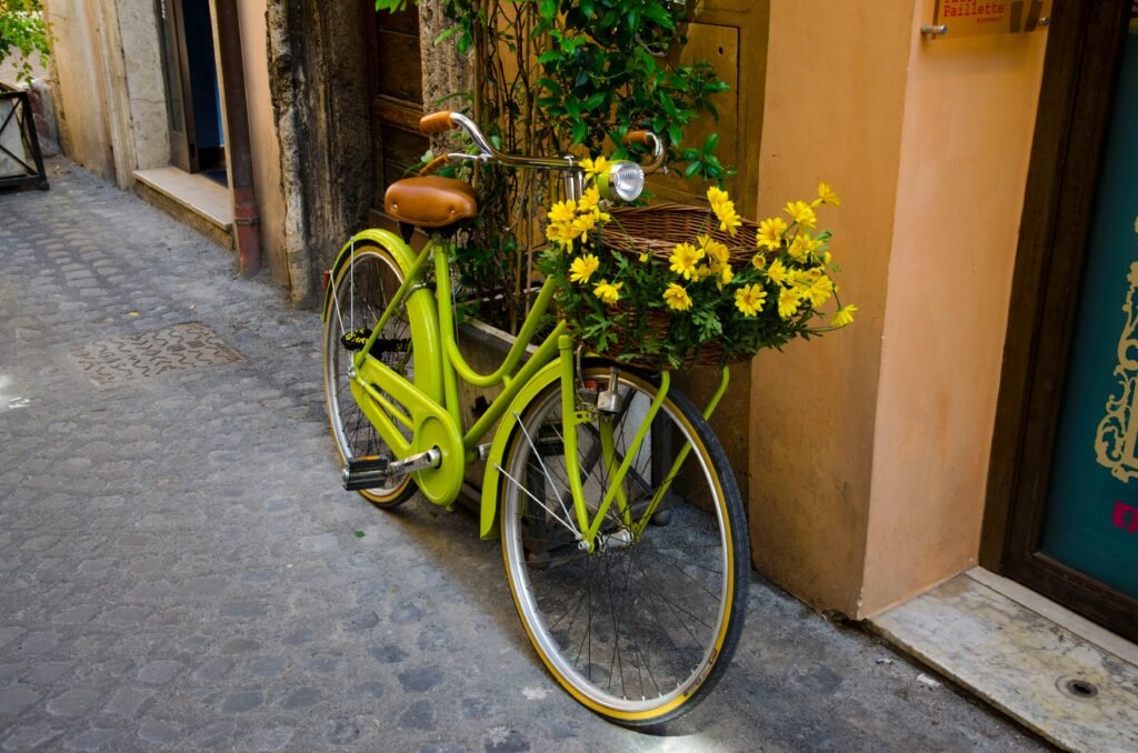 A vibrant green bicycle with a basket of blooming yellow flowers on a cobblestone street. To show bicycle-friendly cities